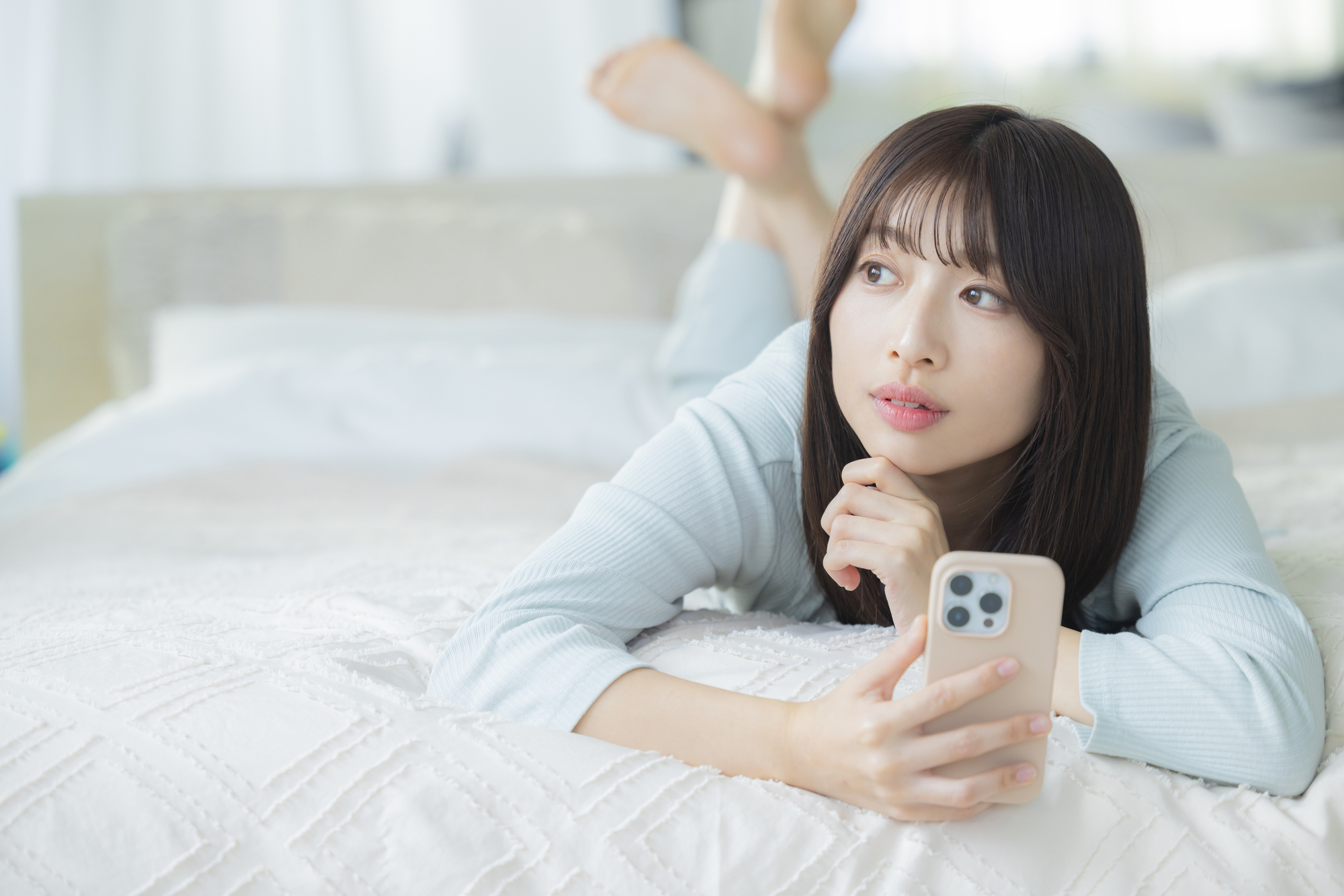 ベッドでスマートフォンを見る女性