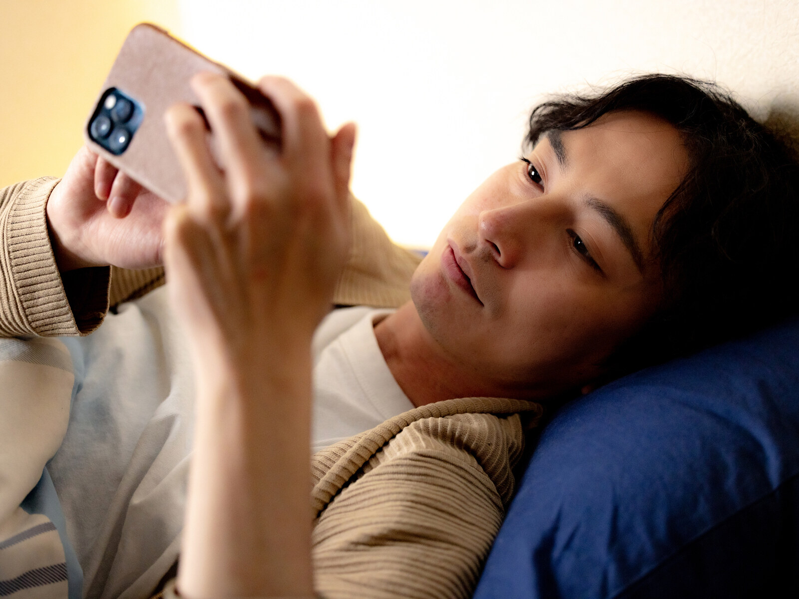 ベッドでスマートフォンを見る男性